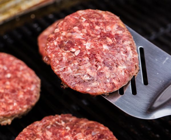 Grilled ground beef pattie burger on spatula against bbq